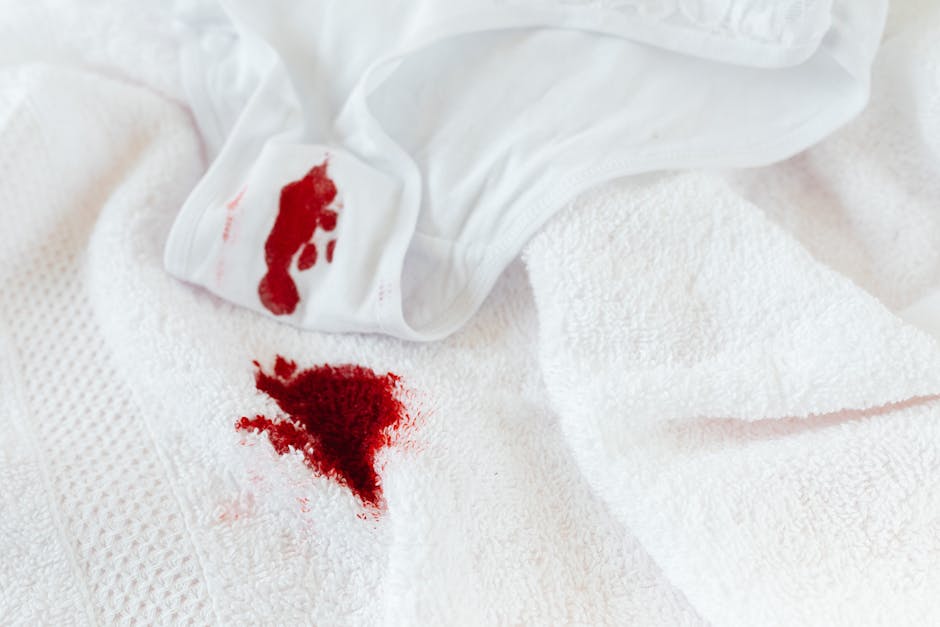 A close-up of a bloodstain on a white textured towel, with a bloodstained white cloth partially draped over the towel. The towel appears to be a soft, plush material, reflecting typical household or h